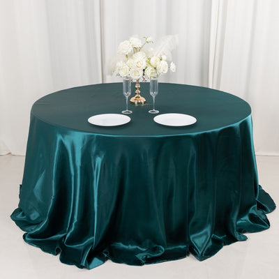 Elegant round table set with teal satin cloth, plates, and floral centerpiece.