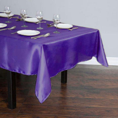 Purple satin tablecloth draped over a wooden table set for dinner.