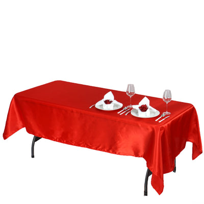 Red satin tablecloth draped over a table set for dining with plates and glasses.