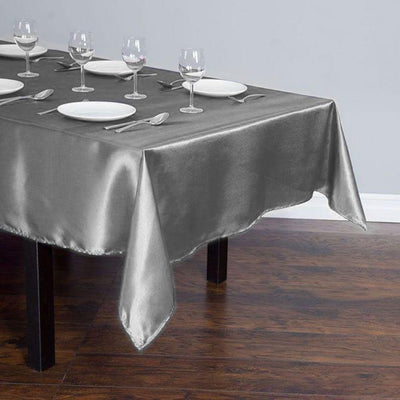 Silver satin tablecloth draped over a wooden table with plates and glasses set.
