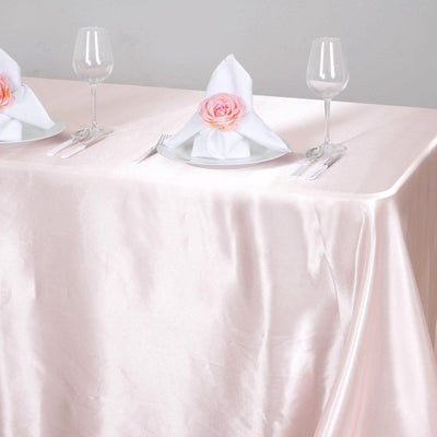 Elegant table setting with pink satin tablecloth and decorative napkin rose.