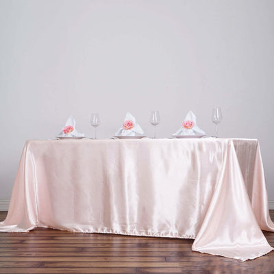 Elegant pink satin tablecloth draped on a table with napkins and glasses.