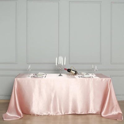 Elegant pink satin tablecloth draped over a dining table with candles and wine.