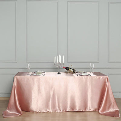 Elegant pink satin tablecloth draped over a dining table with candles and wine.