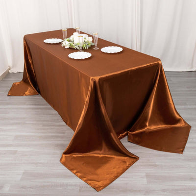 Elegant brown satin tablecloth draping over a table with white plates and candles.