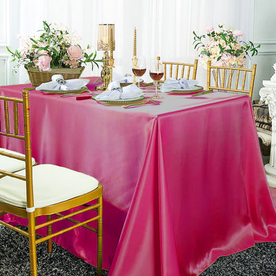 Elegant pink tablecloth draped over a dining table set with flowers and wine glasses.