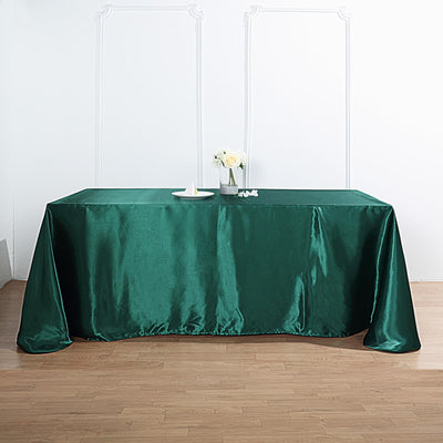 Green satin tablecloth on a wooden table with floral centerpiece.