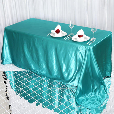 Teal satin tablecloth draped over a table set with plates and glasses.