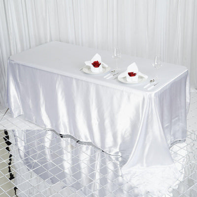 Elegant white table with satin tablecloth set for two with rose and glassware.