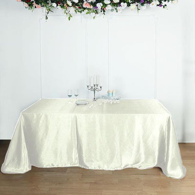Elegant ivory tablecloth draped over a table with candle and glassware.