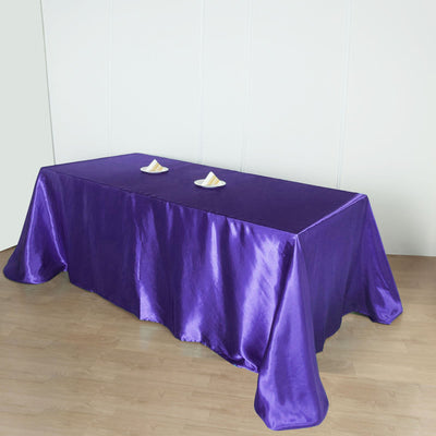 Purple satin tablecloth draped over a wooden table with two decorative items.