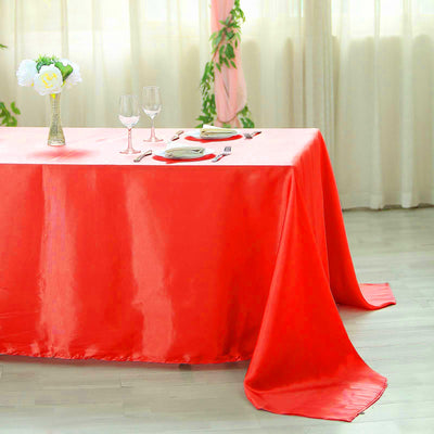 Red satin tablecloth on a dining table set with glasses and plates.