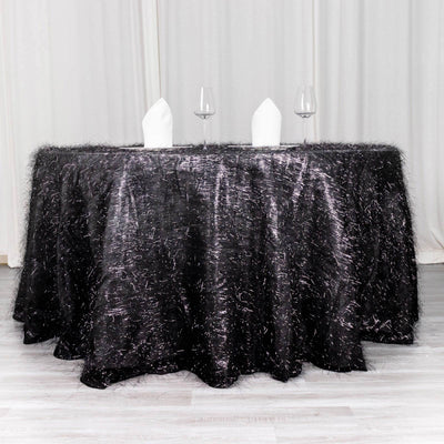 Black textured tablecloth draped over a round table with white napkins and glasses.