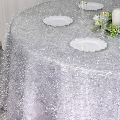 Silver textured tablecloth draped over a round table with white plates and decor.