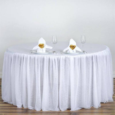 Round table with white tablecloth, napkins, and glasses set for dining.