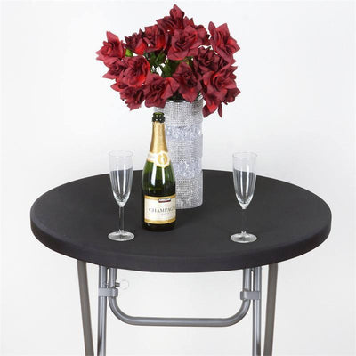 Round black table with champagne, flutes, and a vase of red flowers.