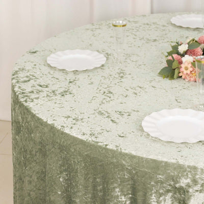 Green textured tablecloth with white plates and floral centerpiece on a round table.