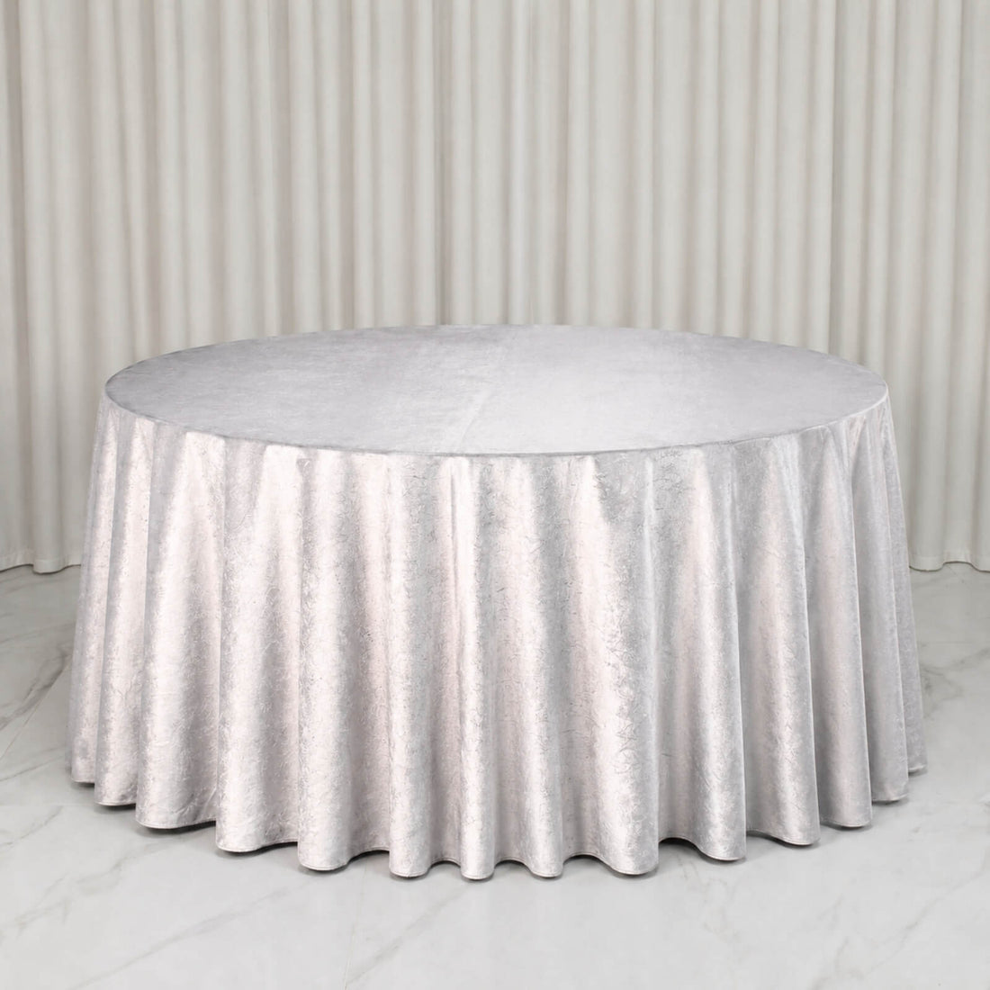 Round silver table with elegant metallic tablecloth and draped backdrop