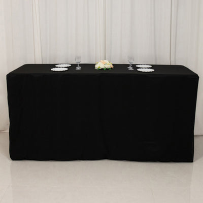 Black tablecloth draped over a table with plates and glasses set on top.