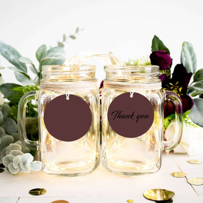 Mason jars with "Thank you" tags, surrounded by greenery and decor.