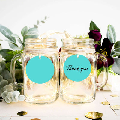 Mason jars with "Thank you" tags surrounded by greenery and decorative elements.