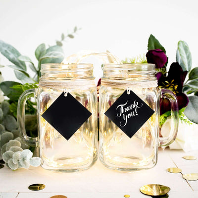 Mason jars with "Thank You!" tags surrounded by greenery and decorative elements.