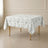 White tablecloth with dusty sage green French toile pattern on a wooden table.