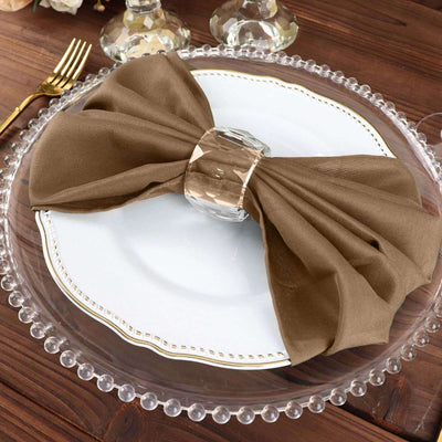 Elegant brown napkin with crystal ring on a white plate, styled for a dining table.