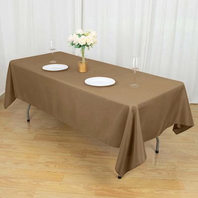 Brown tablecloth draped over a table set for dinner with plates and a flower vase.