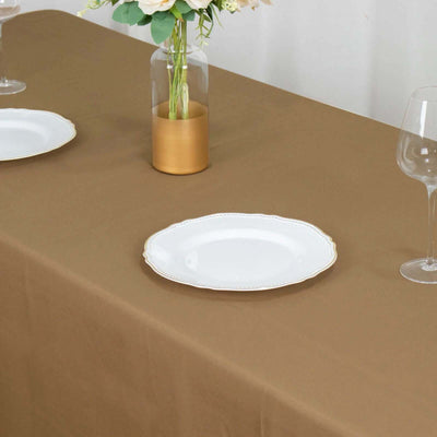 Elegant white plate on a brown tablecloth with a vase and wine glass.