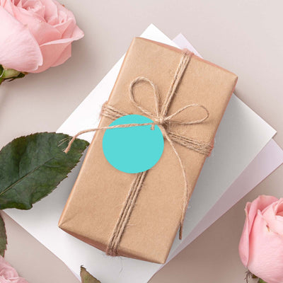 Brown gift box with twine and a teal tag, surrounded by pink roses.