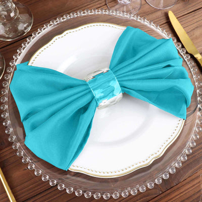 Teal fabric napkin tied in a bow on a decorative plate.