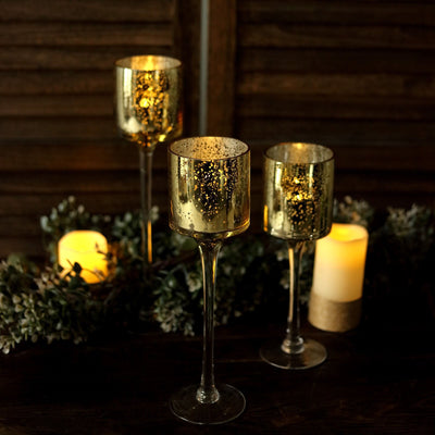 Elegant gold mercury glass candle holders on a rustic table with greenery and candles.