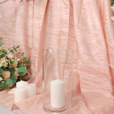 White candles in a glass holder on a pink textured fabric backdrop.