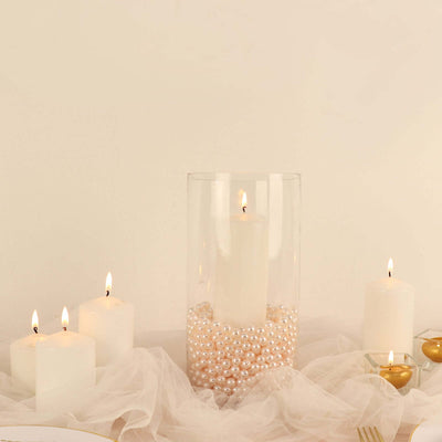 Decorative candles with pearls in a glass holder on a soft fabric background.