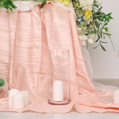 Clear glass vase with white candles on a pink tablecloth.