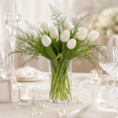 White tulips centerpiece in glass vase with candles and pearls on elegant table