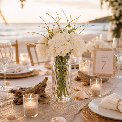 Beach wedding table centerpiece with white flowers, candles, and driftwood