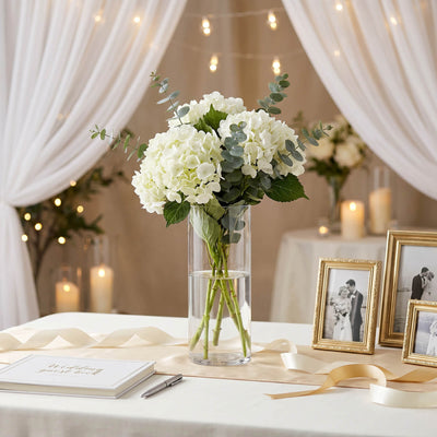 Elegant white hydrangea wedding centerpiece in glass vase with candles and ribbons