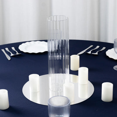 Clear ribbed vase centerpiece on a navy table setting with candles and plates.