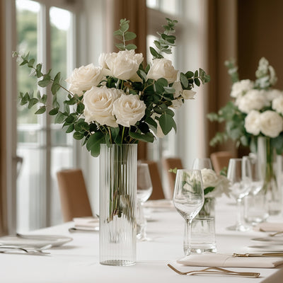 Elegant white roses in a tall glass vase on a dining table.