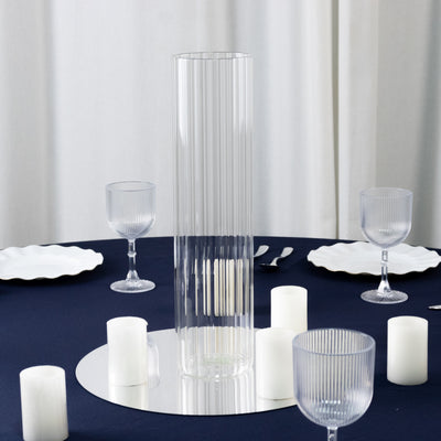 Clear ribbed glass vase on a dark table with candles and glassware.
