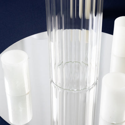 Clear glass vase on a mirrored surface with white candle holders.