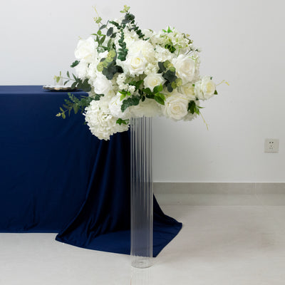 White floral arrangement in a clear vase on a table with a blue cloth.