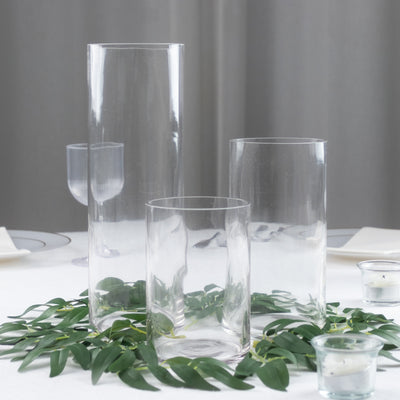 Three elegant glass vases surrounded by greenery on a dining table.