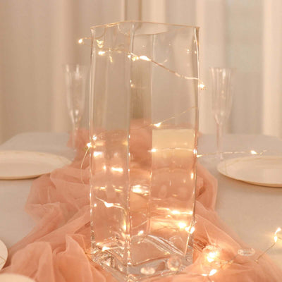 Clear glass vase with fairy lights on a table setting.