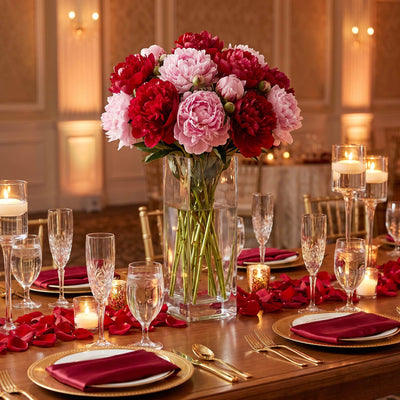Elegant floral banquet table with pink and red peonies, candles, and gold tableware