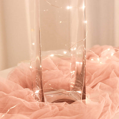 Clear glass vase surrounded by soft pink fabric and fairy lights.