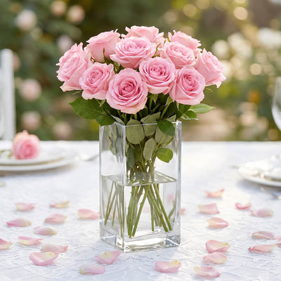Pink rose bouquet in a glass vase on a white table with scattered petals