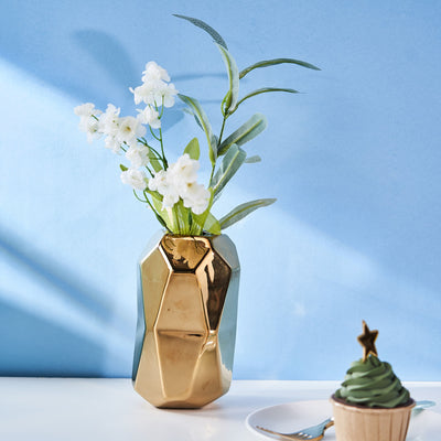 Geometric gold vase with white flowers against a blue background.